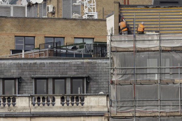Two workmen in high viz orange jackets on scaffolding on a building, City of London, England, United Kingdom
