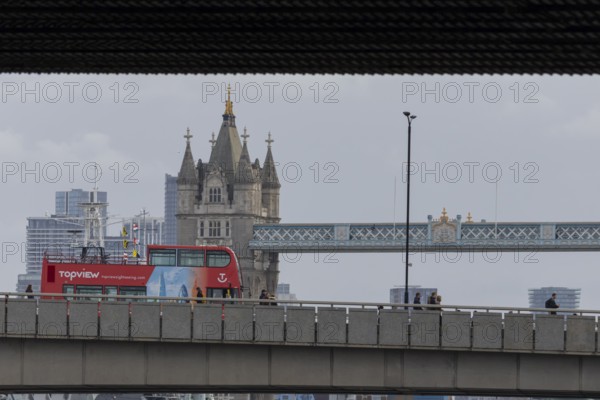 Red double decker bus driving over a bridge with Tower bridge in the background, City of London, England, United Kingdom