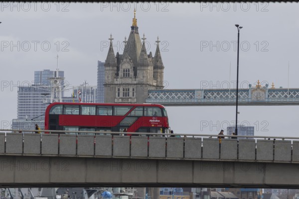 Red double decker bus driving over a bridge with Tower bridge in the background, City of London, England, United Kingdom