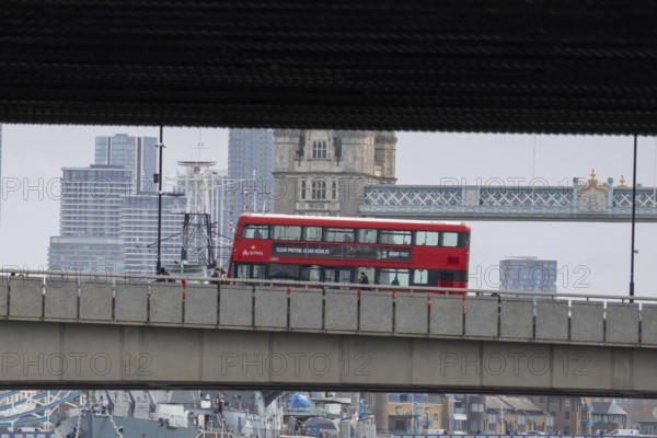 Red double decker bus driving over a bridge with Tower bridge in the background, City of London, England, United Kingdom