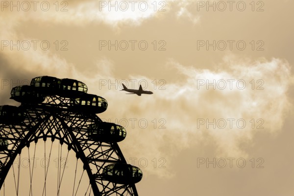 The London Eye wheel with a jet aircraft flying behind at sunset, City of London, England, United Kingdom