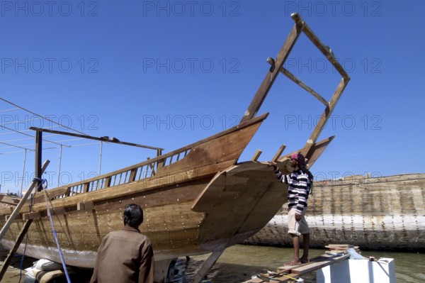 New dhow under construction, shipyard in Sur, two boat builders inspect the work progress, Sur, Oman