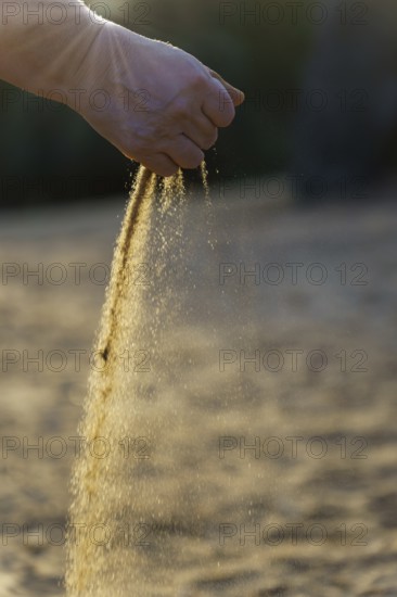 Hand pouring sand at sunset, symbolizing the passage of time and the ephemeral nature of life