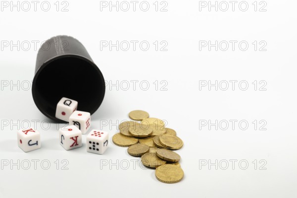 Poker dice and coins spilling from a dice cup on a white background represent gambling and risk-taking