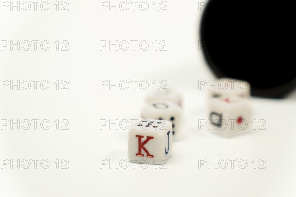 Poker dice showing king, jack, queen and ten on white background with black cup