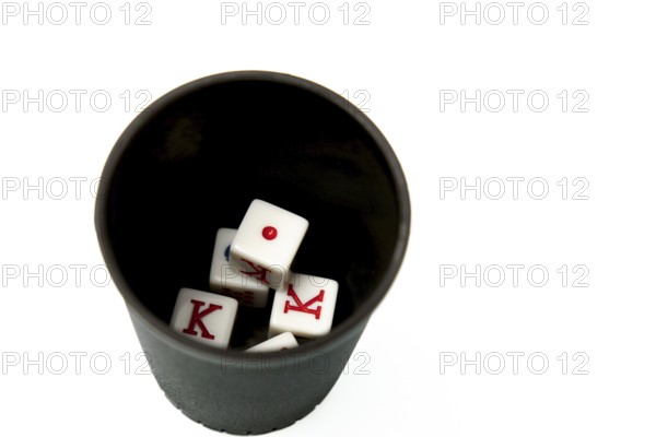 Four white dice showing king and one resting in a black dice cup on a white background, suggesting gambling and games of chance