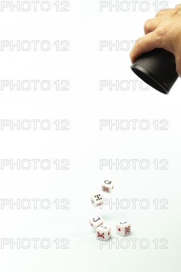White poker dice with black and red markings roll out of a black cup held by a dealer on a white background