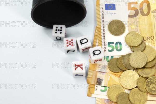 Poker dice spilling from a black cup onto a pile of fifty euro banknotes and coins, symbolizing gambling, risk, and investment