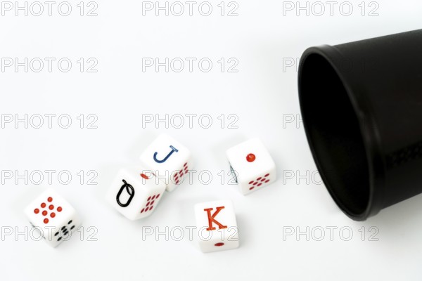 Poker dice spilling from a black dice cup onto a white background, representing gambling and games of chance