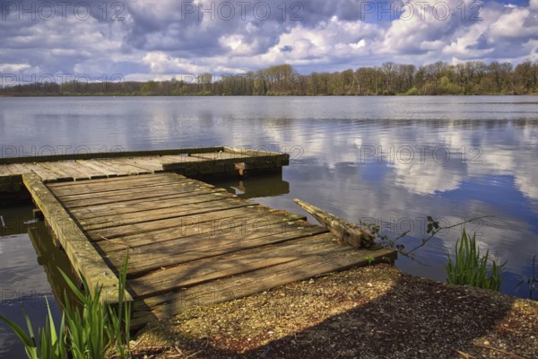 Old wooden jetty on the lake (Krickenbecker Seen) with clouds reflecting on the water, Nettetal