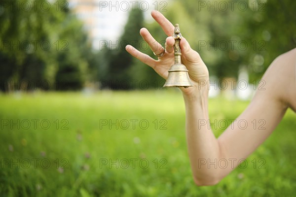 A hand gracefully holds a singing bell in a vibrant green garden, with soft sunlight filtering through nearby trees. The tranquil setting enhances the calming energy of the bowl