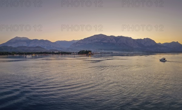 Seascape sunset panorama over the Mediterranean Sea near Kemer, Turkey. Panoramic view to the moonlight beach at dusk and a lone boat cruises across the calm water towards the majestic mountains