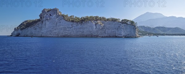 Vibrant seascape panorama with beautiful Turkish mediterranean coastline lined with tree covered cliffs and hills under a clear sky in Kemer, Turkey