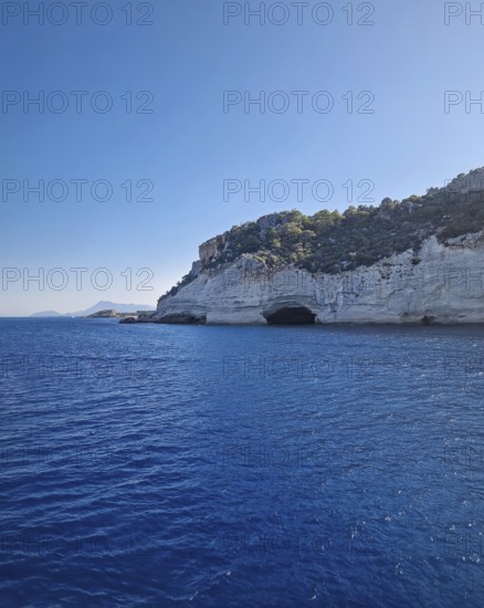 Vibrant seascape with the Pirate Cave in Kemer, Turkey. Beautiful Turkish mediterranean coastline lined with tree covered rocky cliffs and hills under a clear sky