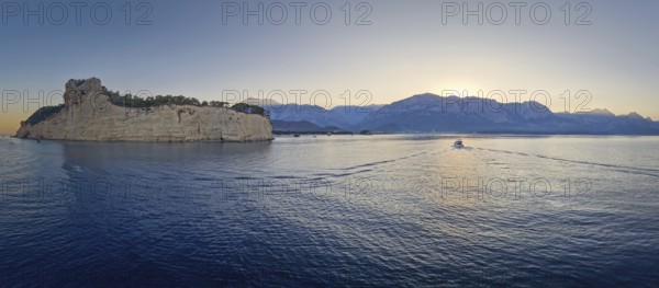 Scenic sunset panorama over Turkish Mediterranean coastline, with majestic Taurus mountains in the background. Boat sailing on the calm sea water in Kemer, Turkey