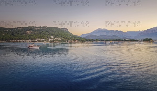 Seascape sunset panorama over the Mediterranean Sea near Kemer, Turkey. Panoramic view to the moonlight beach at dusk and a lone boat cruises across the calm water towards the majestic mountains