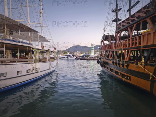 Kemer marina at dusk, filled with multiple docked boats. Lights of the harbor and the resort shoreline reflects on the calm sea water