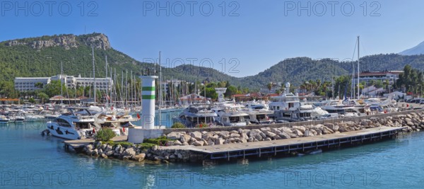 KEMER, TURKEY - JULY 3, 2025 Marina panoramic view with Calis Hill in the background. Rocky pier filled with numerous boats and yachts on the clear turquoise water under a bright blue Turkish sky