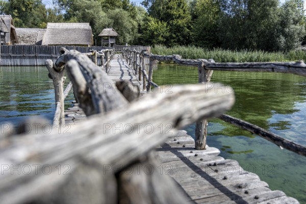 Wooden bridge near huts offers views of green water and dense vegetation, pile dwellings at Unteruhldingen Open-Air Museum on Lake Constance Germany