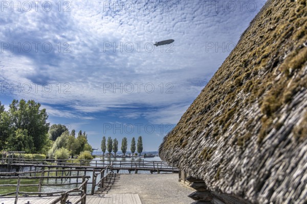 Thatched roof building with a view of trees and clouds in a rural setting, pile dwellings Unteruhldingen Open-Air Museum Lake Constance Germany