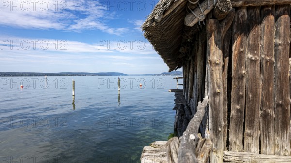 Wooden hut directly on the lake with blue sky and scattered clouds, pile dwellings Unteruhldingen Open Air Museum Lake Constance Germany