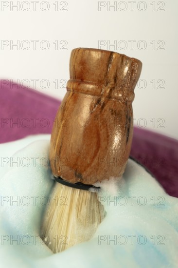 Wooden shaving brush dipped in light blue foam on a purple towel, evoking a sense of luxury and self-care