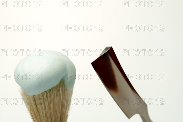 Shaving brush with light blue foam and straight razor on white background, getting ready for skincare routine