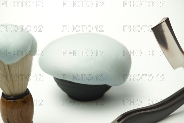 Shaving foam, brush and straight razor are creating a grooming still life on a white background