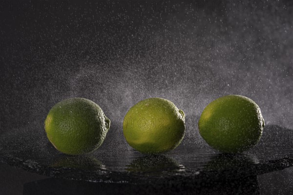 Three limes on a stone slab with drops of water