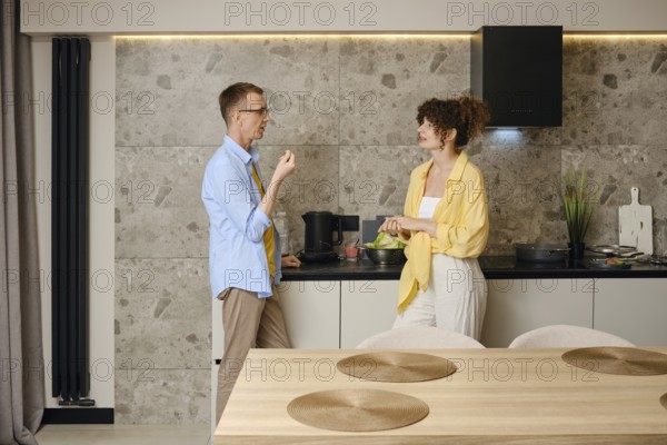 A man and woman are preparing a meal in a contemporary kitchen. They are engaged in conversation and discussing the menu