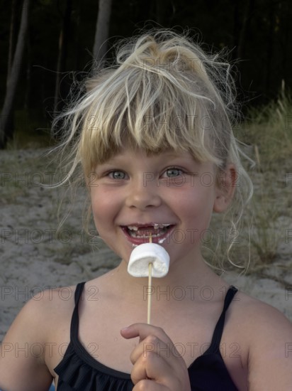 Happy blonde 7 year old Scandinavian girl eating marshmallows outdoors in Ystad, SkÃ¥ne County, Sweden, Scandinavian