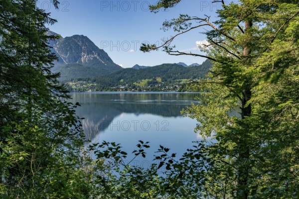 View of Lake Altaussee, framed by trees and mountains under a blue sky, Altaussee, Styria, Austria