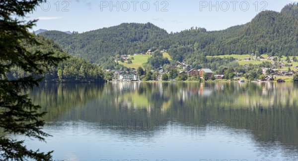 Tranquil lake with surrounding village and wooded hills on the shore reflected in the water, Altaussee, Styria, Austria