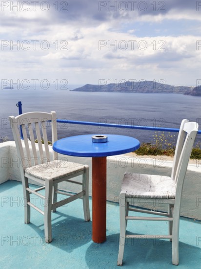Blue table and two white wooden chairs on a terrace with sea view, typical view of the volcanic islands in the caldera, cafÃ©, hiking trail from Fira to Oia, Thira, Santorini, Cyclades, Greece