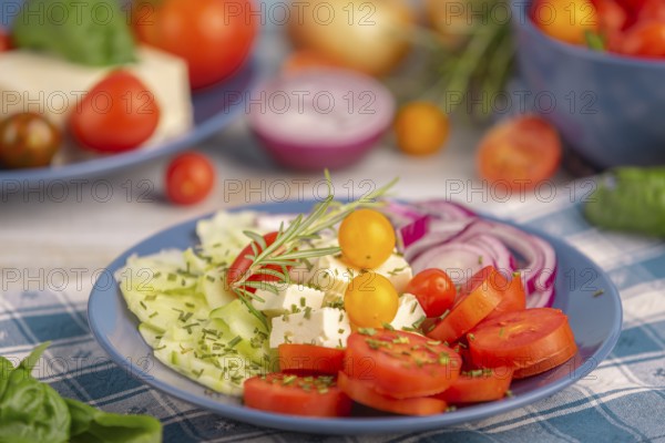 Tomatoes, cucumber, onion and feta on a plate, surrounded by vegetables and herbs