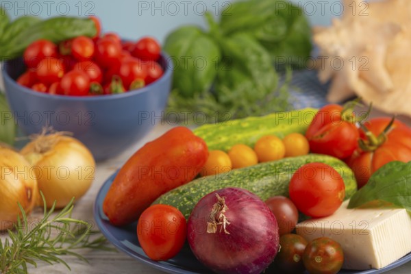 Cucumber, tomatoes, sheep's cheese and onion on a blue plate, surrounded by herbs