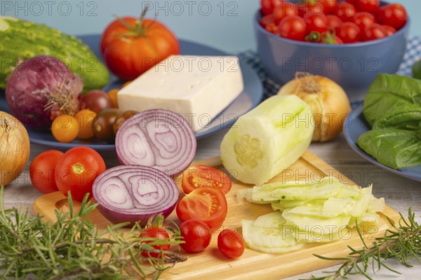 Fresh and sliced vegetables with feta on a wooden board, surrounded by basil and rosemary, rustic cuisine