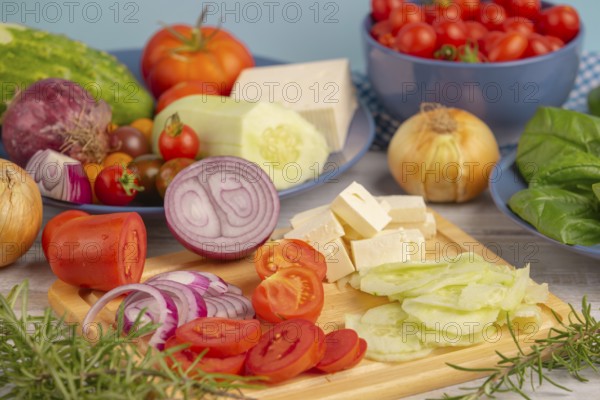 Fresh and sliced vegetables with feta on a wooden board, surrounded by basil and rosemary, rustic cuisine