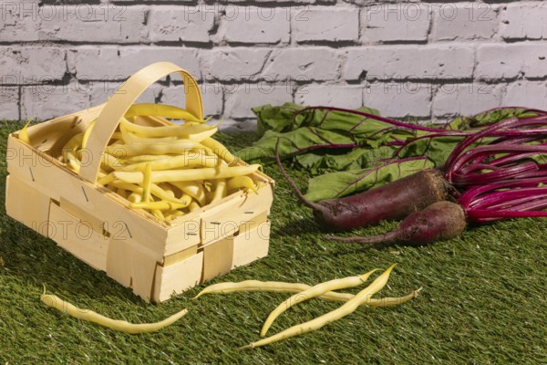 Basket with yellow beans and turnips on a green lawn in front of a wall