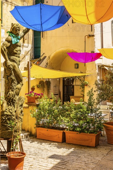 Coloured umbrellas cover a bronze statue in Via Cavour, Capoliveri, Elba Island, Tuscan Archipelago National Park, Tuscany, Italy