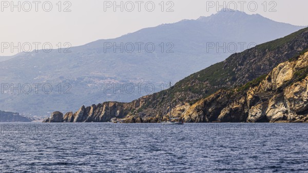 Rocky cliffs near Marina di Campo, in the background in the haze the peak of Monte Capanne, Elba Island, Tuscan Archipelago National Park, Tuscany, Italy