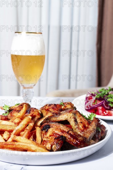 Delicious barbecue chicken wings, with French fries, salad and a refreshing drink, at a cozy table, there are no people