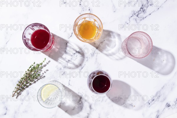 An assortment of drinks on a marble surface, with fresh greenery and shadows, in natural light, top view