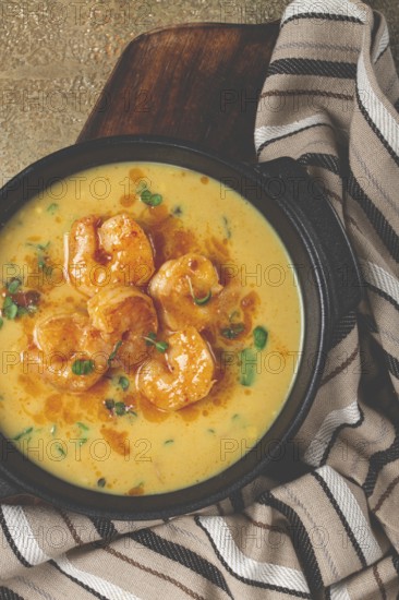 Creamy shrimp curry with spices, garnished with herbs, on a textured background, homemade, no people