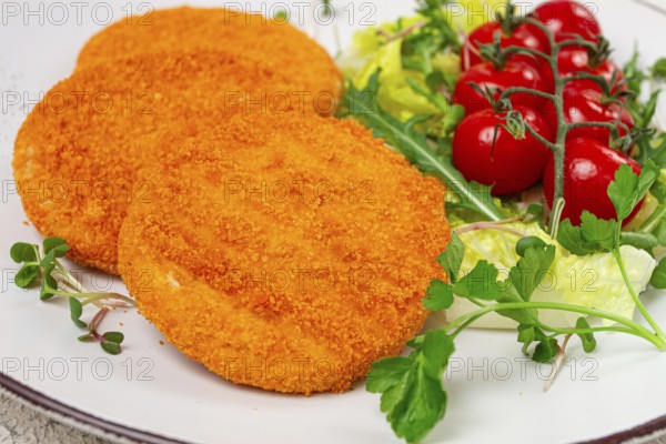 Crispy fried fish cutlets, fish burgers, on a white plate, with fresh lettuce leaves, arugula and cherry tomatoes, homemade, no people