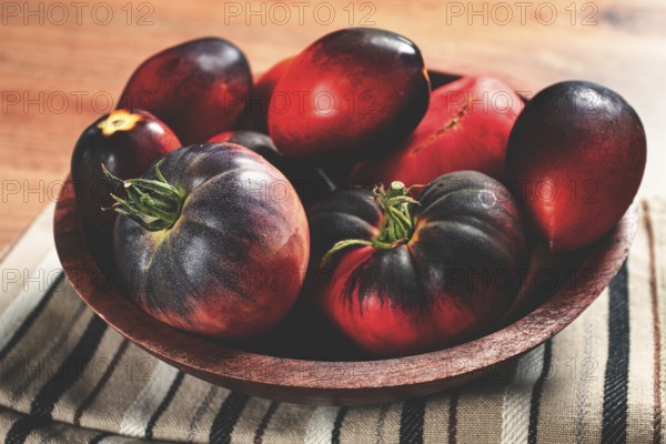 Freshly picked tomatoes, of the Black Beauty variety, in a wooden bowl, close-up, on the kitchen table