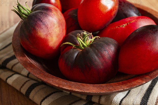 Freshly picked tomatoes, of the Black Beauty variety, in a wooden bowl, close-up, on the kitchen table