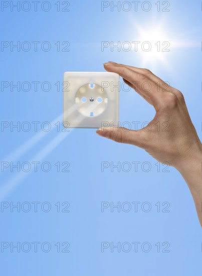 Symbolic solar energy theme showing the sun and sky with human hand holding a electrical socket while sunbeams falling through