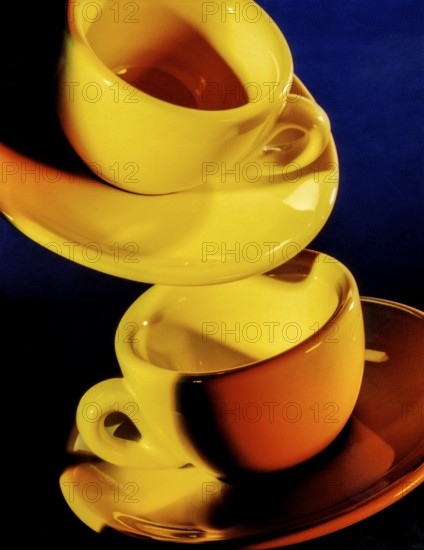 Bright illuminated yellow cups with saucer in dark blue back