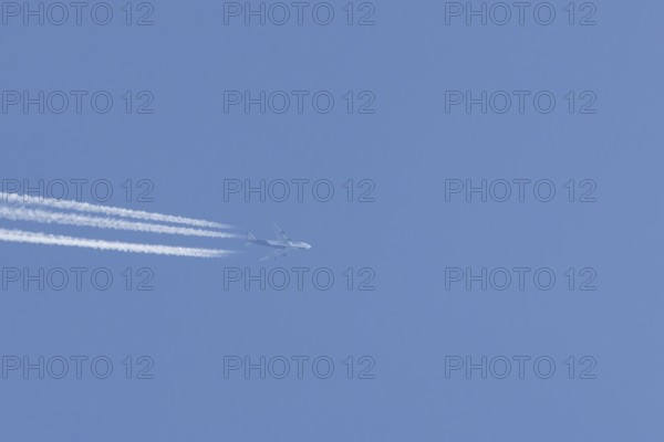 Boeing 747 Jumbo jet passenger aircraft in flight in a blue sky with vapour trails or contrails behind, England, United Kingdom